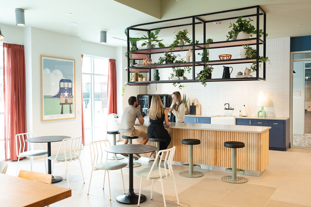 two women and man. they are sitting and standing around a bar talking. decorated with plants and updated kitchen appliances.